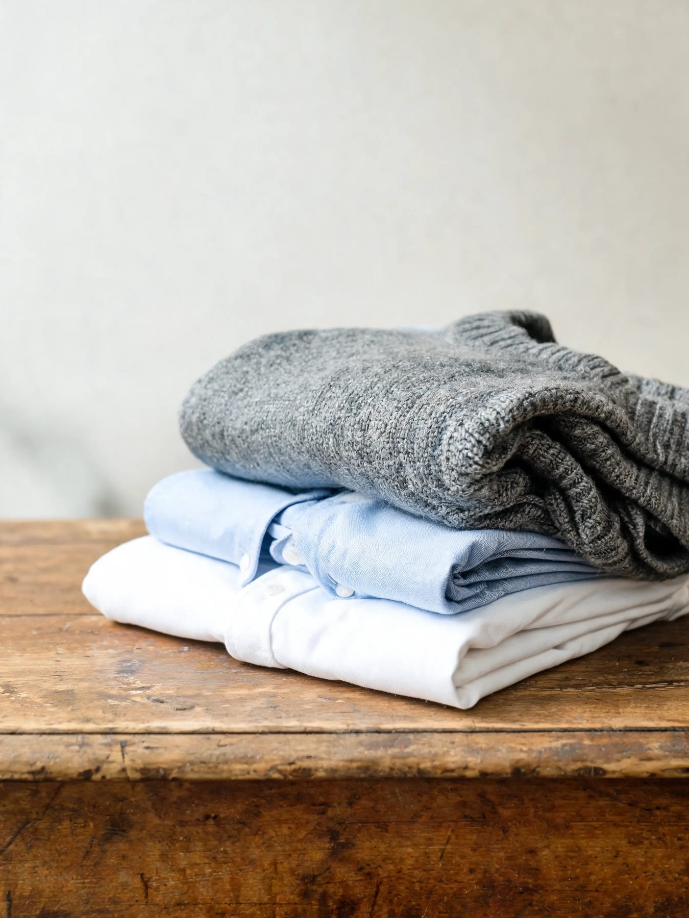 Folded knitwear and shirts stacked on a worn oak table